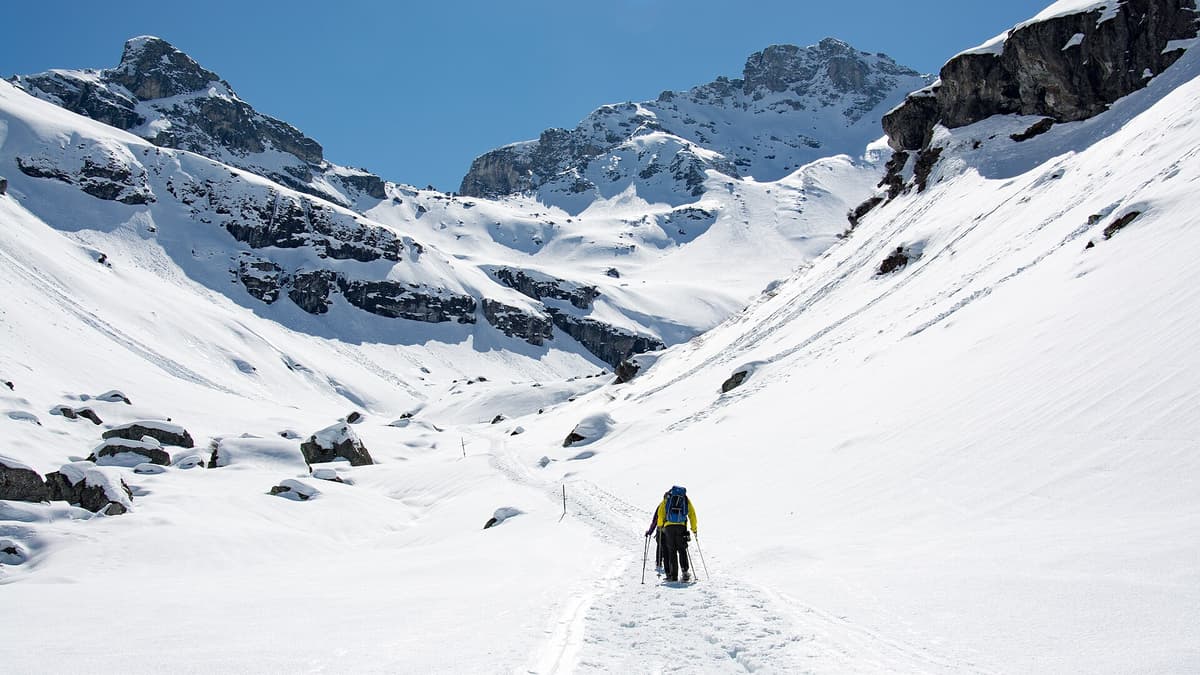 Snowshoe trail winding through deep snow toward a mountain hut