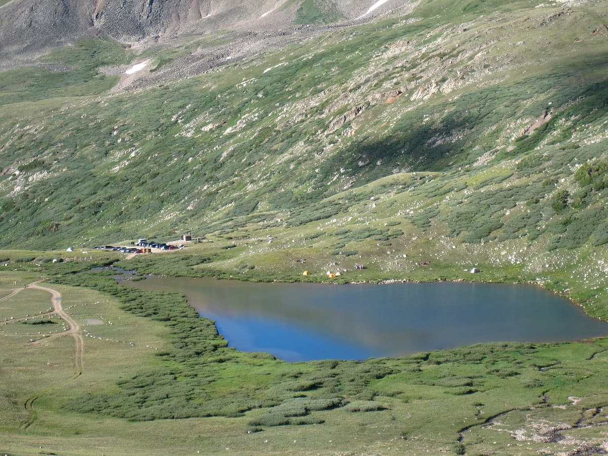 Looking down on Kite Lake, its trailhead parking lot, outhouse, and a scatter of campground tents in a green tundra basin