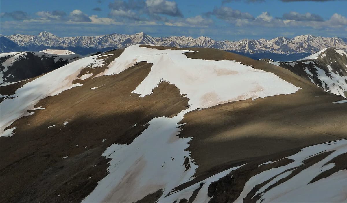 The broad, snow-patched summit hump of Mount Cameron seen from Mount Lincoln, with distant snowcapped ranges on the horizon